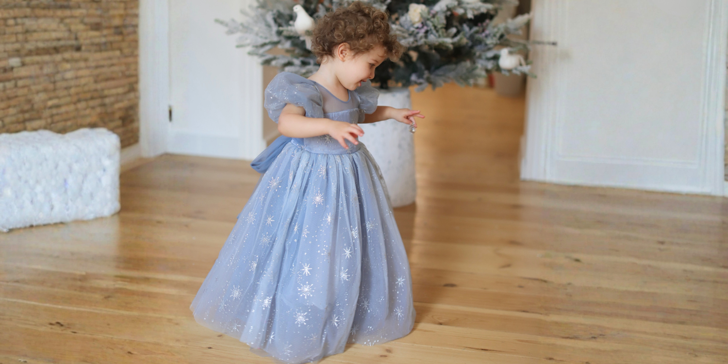Child in a light Petitwishes blue dress with star patterns standing on a wooden floor.