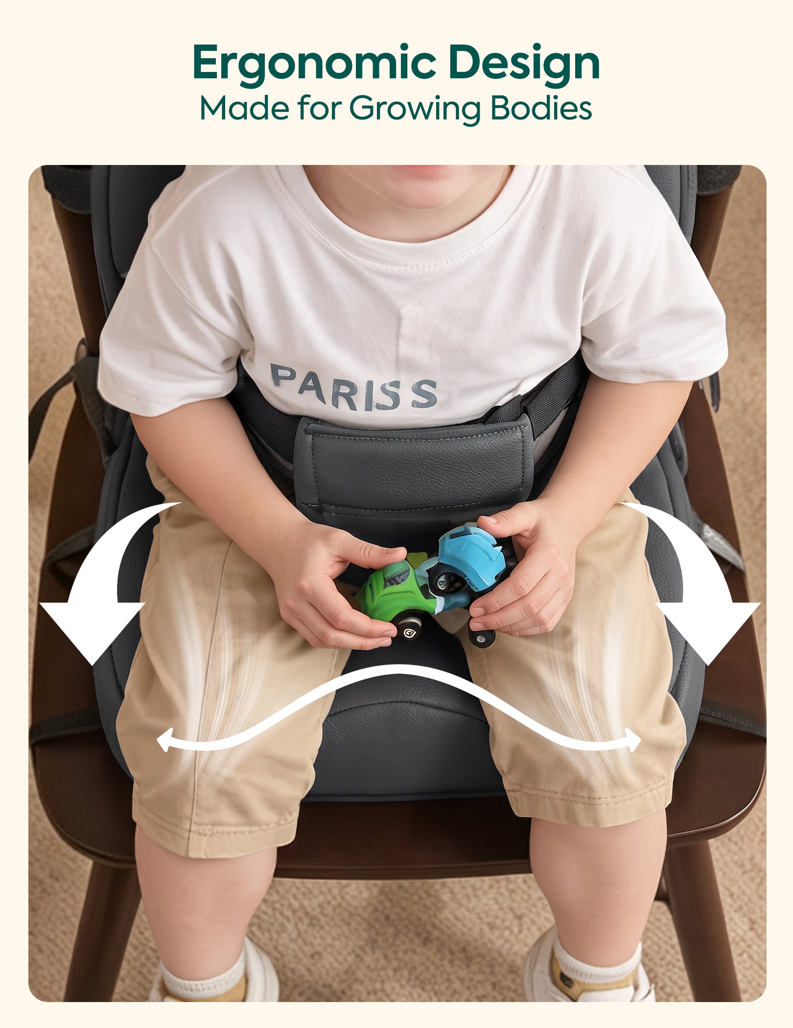 A child wearing a white Paris T-shirt and khaki shorts sits in a dark gray booster seat on a wooden chair, holding a toy car. White arrows and curved lines illustrate side support, with the text 'Ergonomic Design Made for Growing Bodies' at the top.